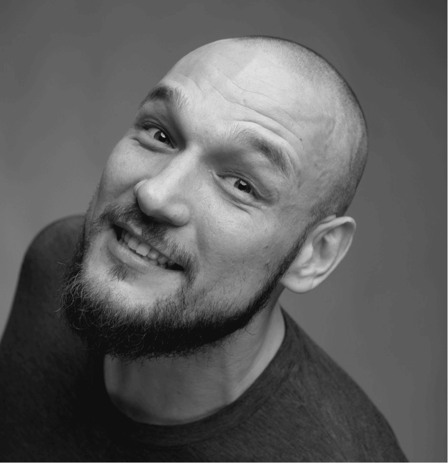 Uśmiechnięty mężczyzna z brodą i blizną na głowie, czarno-białe zdjęcie.